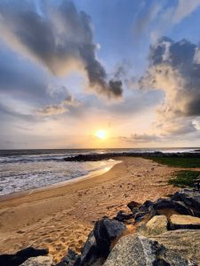 Sunset at Maravanthe Beach, Trasi Beach, Kundapura, India. The sun is a bright yellow color against a cloudy blue sky.