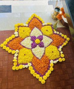 An intricate flower carpet (Pookkalam) on a tile floor near some steps.