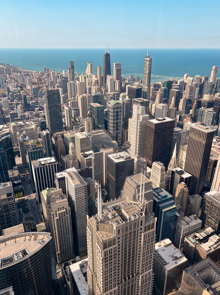 Aerial view of downtown chicago with a dense cluster of skyscrapers and high-rise buildings, extending towards the coastline of lake michigan under a clear blue sky.