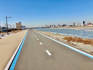 A long, empty road with a blue line stretches through Osaka's winter landscape, alongside the Yamato River under clear skies.