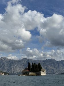 A church in the middle of the lake in Kotor, under a cloudy sky.