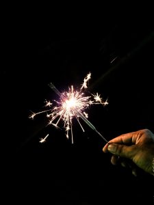 A hand holding a lit sparkler against a dark background.