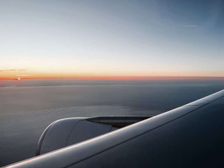 The sun sets behind the clouds just beyond a airplane wing.