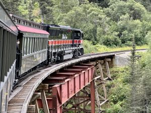 View larger photo: White Pass Railway in Skagway crossing a train bridge over a river.