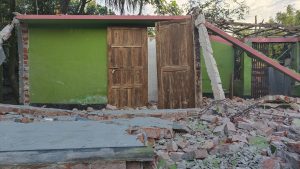 View larger photo: A collapsed house with debris scattered around, showcasing the devastation caused by the earthquake.