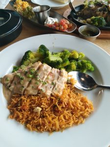 A plate with a sliced chicken breast with a light gravy on it, a serving of fried rice, and a serving of broccoli. 