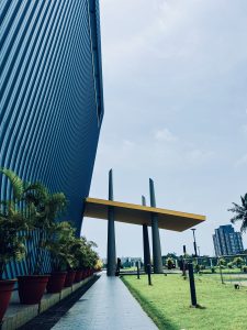 A highrise in a cyberpark with a covered walkway, potted trees, and a green lawn. 