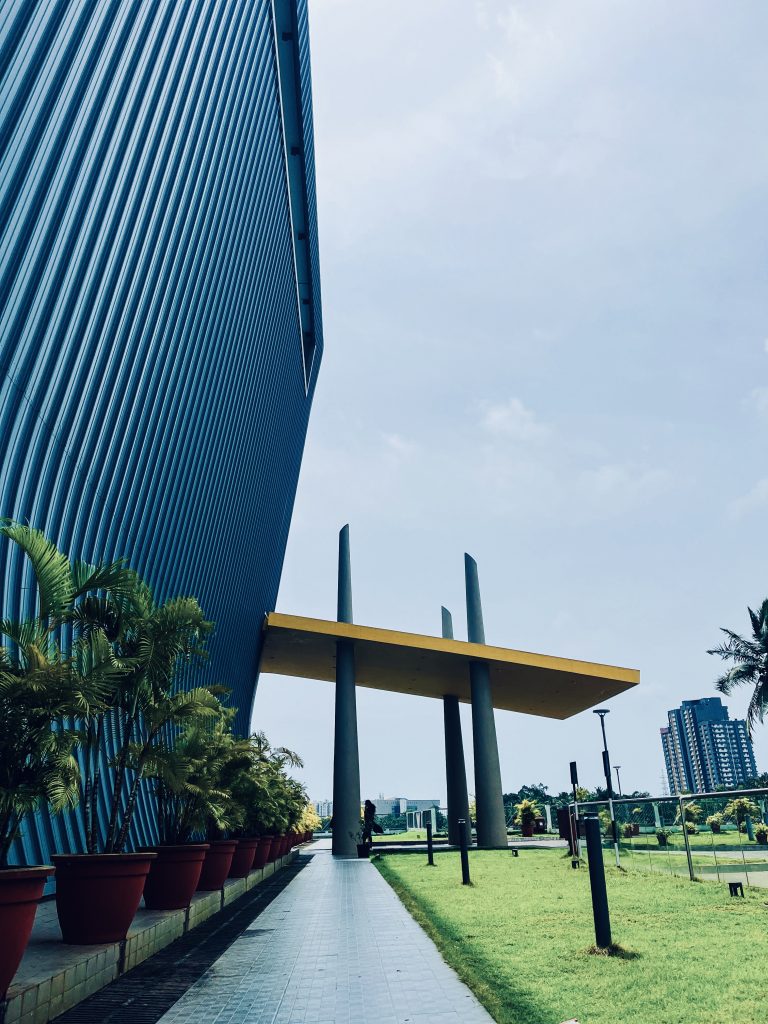 A highrise in a cyberpark with a covered walkway, potted trees, and a green lawn.