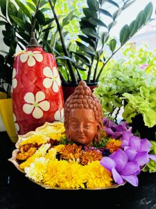 View larger photo: Head of the Buddha in a bowl of flowers, a large vase next to it.