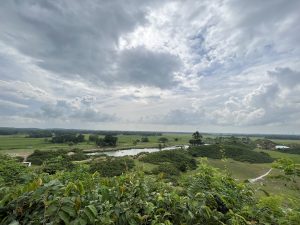  Long view across green countryside with cloudy skies above.