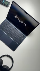 Top view of a MacBook Air M3, a laser distance meter and a pair of headphones on a white table.