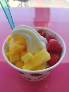 View larger photo: A paper cup of frozen yogurt with fresh fruits on a glossy pink surface.