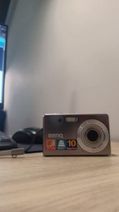  An old generation digital camera placed on the table near a black computer keyboard.