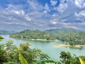 Long view of a lake with islands covered in trees under a blue cloud filled sky.