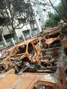 A large number of rusty old car wrecks parked alongside a modern white building.