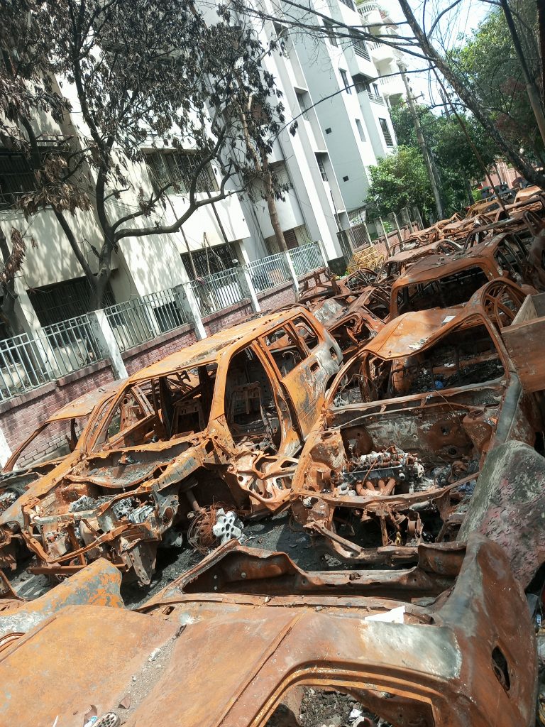 A large number of rusty old car wrecks parked alongside a modern white building.