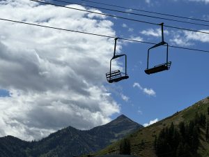 View larger photo: Ski lift during the summer with mountains and a cloudy sky in the background.