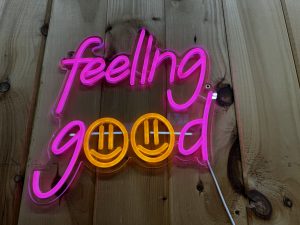 View larger photo: Neon-like sign that reads "Feeling Good" on a brown wooden wall. The two o's are smiley faces.