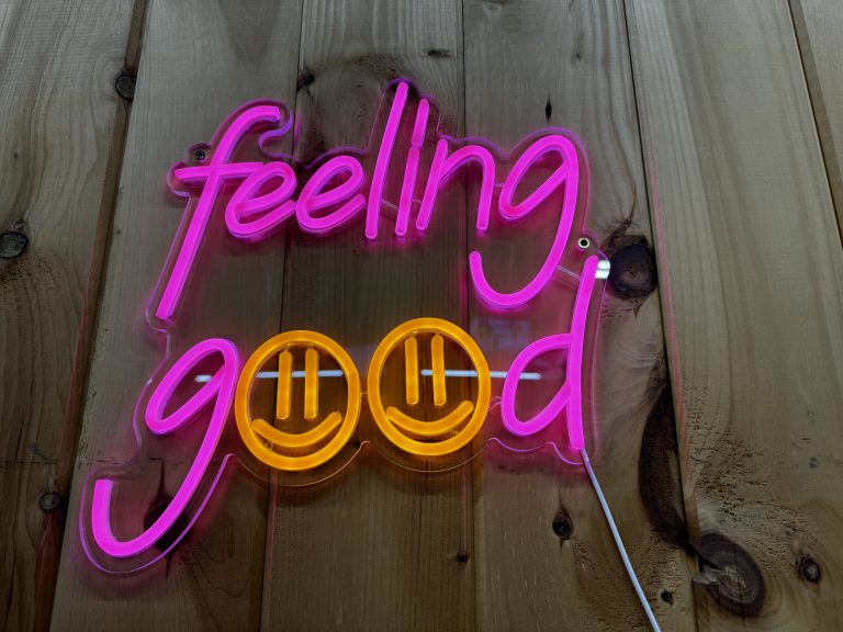 Neon-like sign that reads “Feeling Good” on a brown wooden wall. The two o’s are smiley faces.