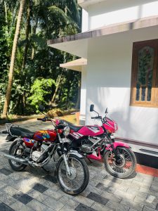 View larger photo: Two colorful vintage motocycles parked near a white stone building.