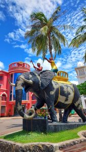 View larger photo: Elephant and keeper statue with a coconut tree and several buildings in the background in Krong Siem Reap, Cambodia.