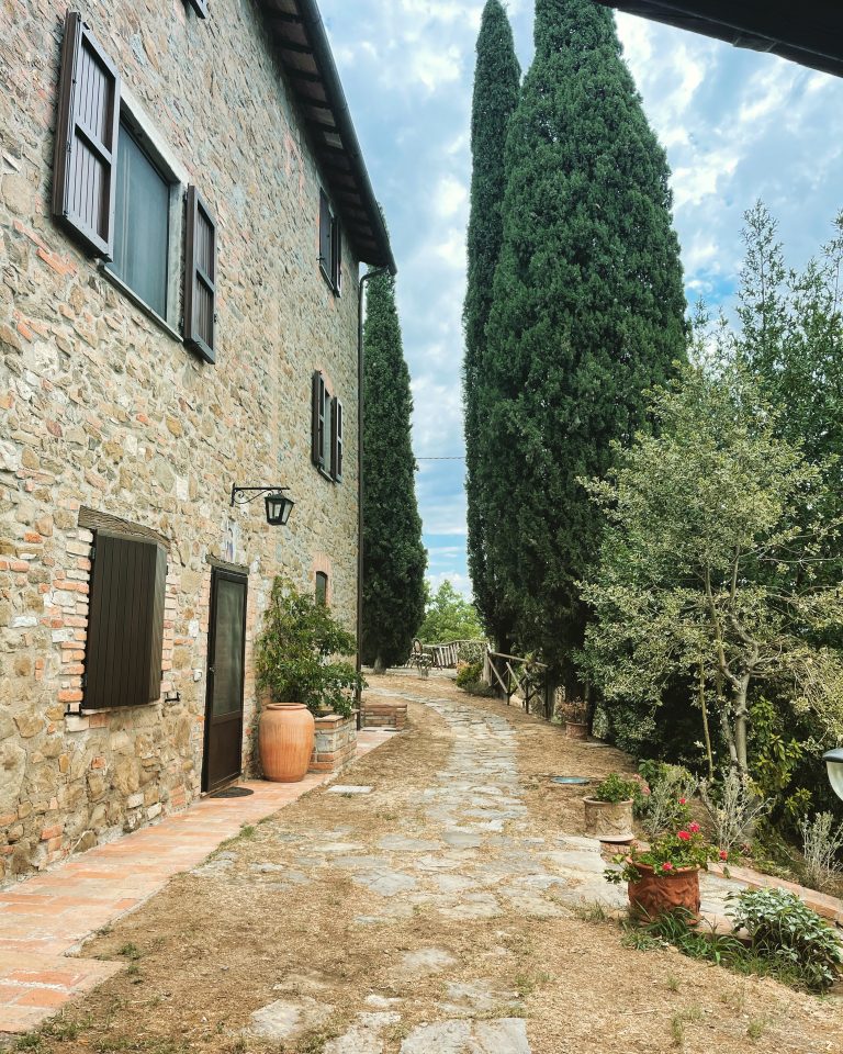 The side of a villa in Umbria, Italy, with a path leading into the garden. Large poplar trees can be seen in the background.