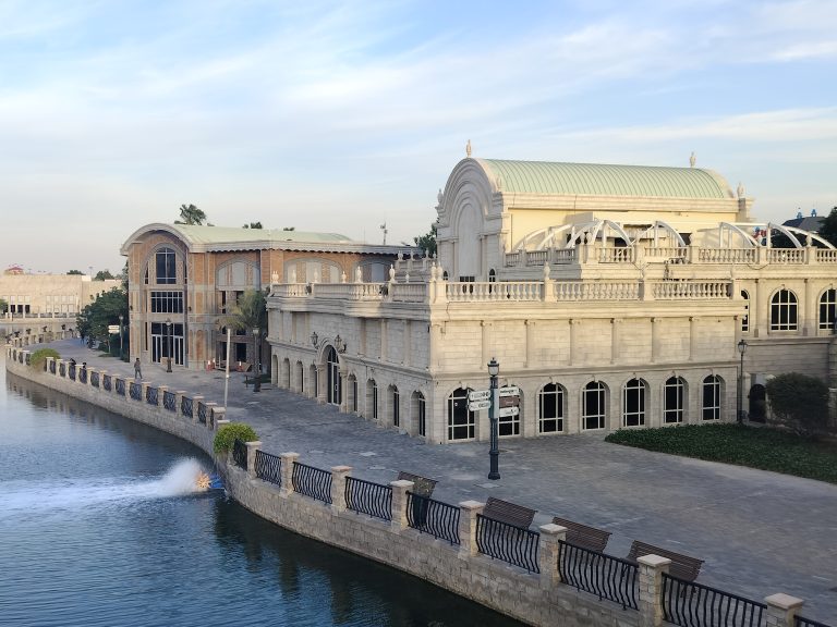 Riverland, Dubai. Large stone building witha. walkway by water.