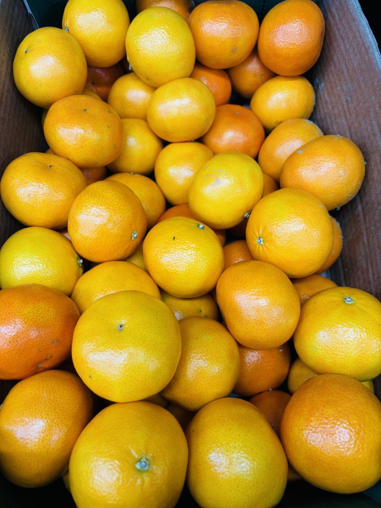 A cardboard box filled with numerous bright orange mandarins.