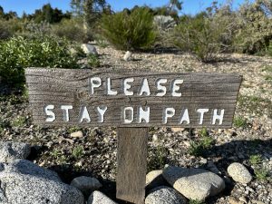 A wooden sign that says, “Please stay on path.”