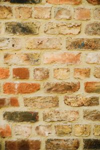 View larger photo: Close-up of an old brick wall with a mix of light and dark orange bricks, some showing signs of weathering and age, set in pale yellow mortar.