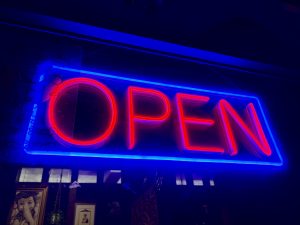 A vibrant blue and red neon “open” sign inside of a restaurant’s window, shot at night.