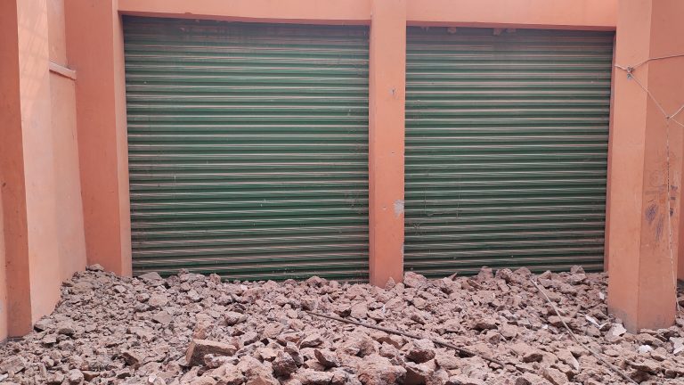 A pile of rubble in front of a broken shop, showcasing debris and remnants of the building’s structure.