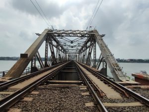 View larger photo: View of a railway track on an iron bridge spanning over a river, with a cloudy sky in the background.