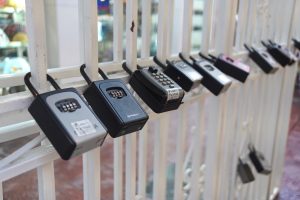 A row of combination lock boxes is attached to a white metal gate. Each lock has a numeric keypad or dial for securing access. 