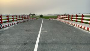 A narrow road with a white line marking its center stretches across a small bridge with red and white painted railings. 