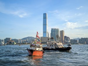 Two boats in the harbour in Hong Kong. Tall buildings and mountains are in the background.