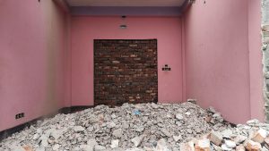 View larger photo: A pink building featuring a door, set against a backdrop of rubble, representing a broken house.