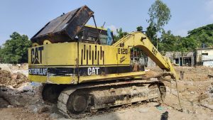 A yellow and black excavator rests on a dirt pile, showcasing its powerful machinery against a clear sky backdrop.