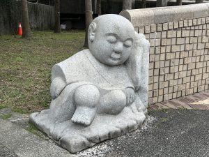 View larger photo: A stone Buddha statue sleeps against a stone wall with trees and grass behind it.