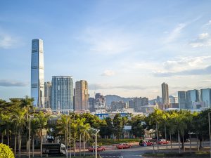 Skyscrapers in hongkong. Mountains in the background. A row of taxis and palm trees in the foreground.