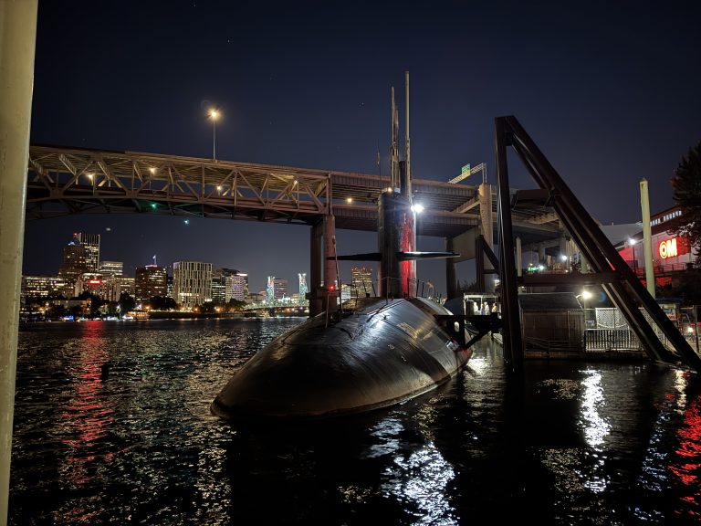 The front of the USS Blueback (SS-581) in the Willamette River in Portland, Oregon at night. The Marquam Bridge is visible in the background.