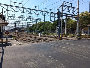 View larger photo: A level railroad crossing with multiple parallel train tracks running beneath a network of overhead electrical lines. To the left, a no-entry sign is visible. The surroundings feature greenery and a few structures. The location is marked as Emplasemen Stasiun Lempuyangan Jogjakarta.