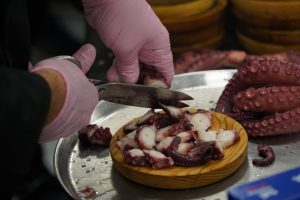 View larger photo: Hands in pink gloves of a cook preparing pulpo a feira, cutting octopus with scissors