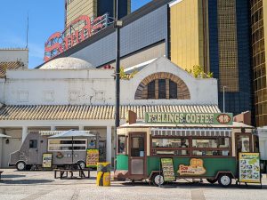 An ice cream truck in front of city buildings, the back one says "Sands." 