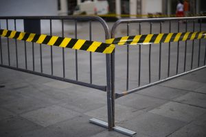 View larger photo: A metal barricade on a paved surface with black and yellow caution tape wrapped around it, indicating a restricted or warning area.