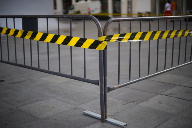 A metal barricade on a paved surface with black and yellow caution tape wrapped around it, indicating a restricted or warning area.