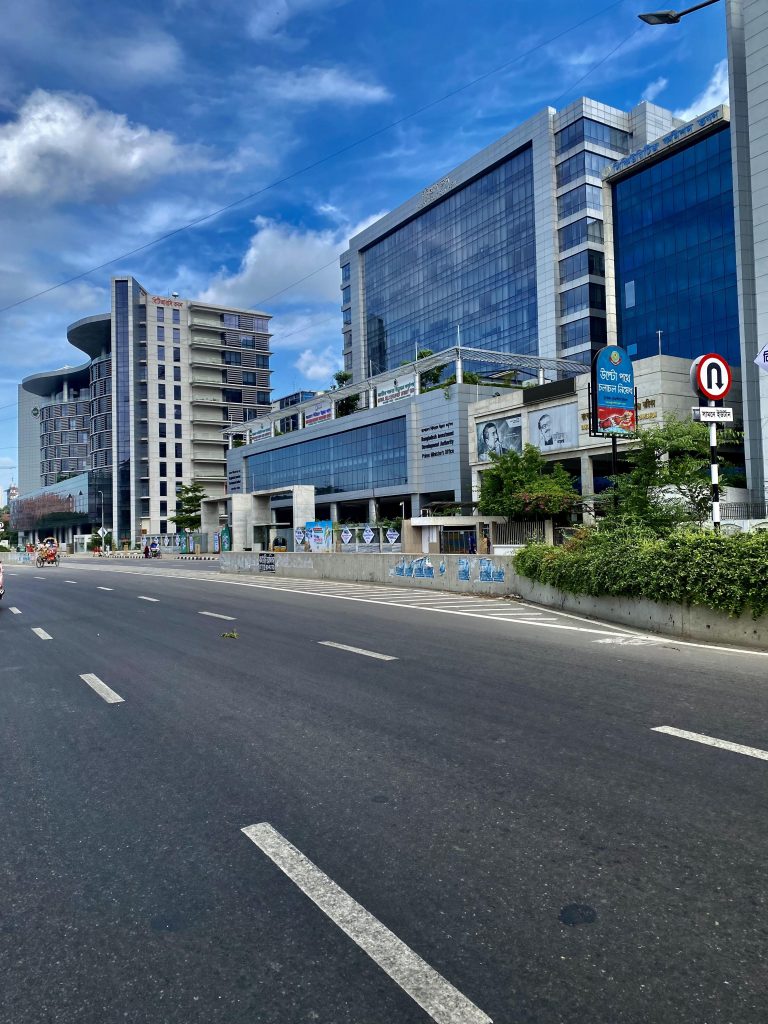 A wide, empty road with clear markings stretches alongside modern, multi-story glass and concrete buildings