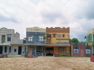 Colorful buildings from the old west in the USA. There's a dirt road in front of them and a cloudy sky.