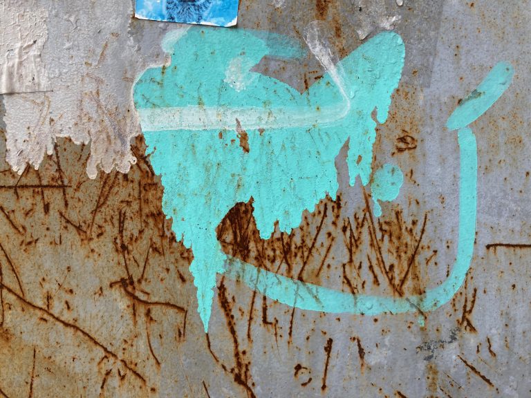 A textured white wall with some blue greenish paint marks and rusty scratches.