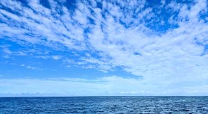 Photo of a blue ocean against a blue lightly cloudy sky.